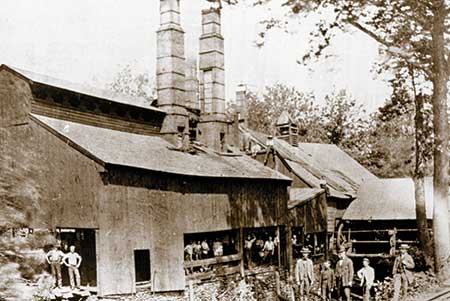The original mill building, photographed in 1887. The photo was taken before the old mill was retrofitted as a puddling operation. C. L. Huston, A. F. Huston, H. B. Spackman and Dr. Charles Huston (bowler hat) are the last four men standing in the lower right corner. 